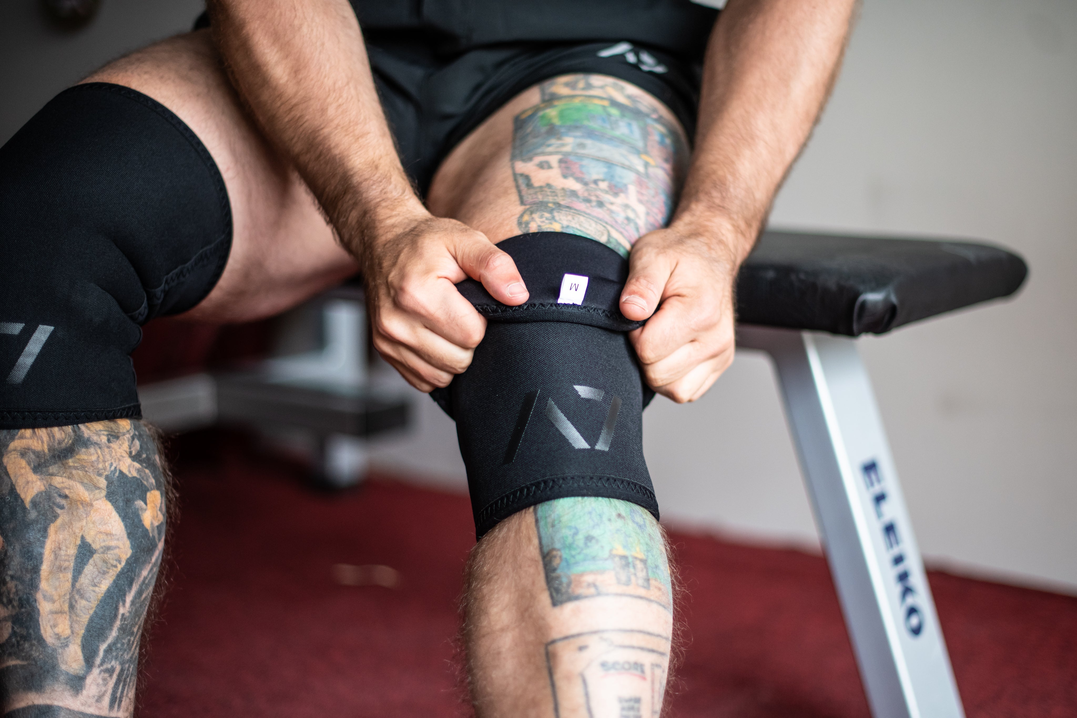 Both A7 Stealth Stiff CONE Knee Sleeves on Lifters knees displaying the pair of sleeves and putting them on knees.