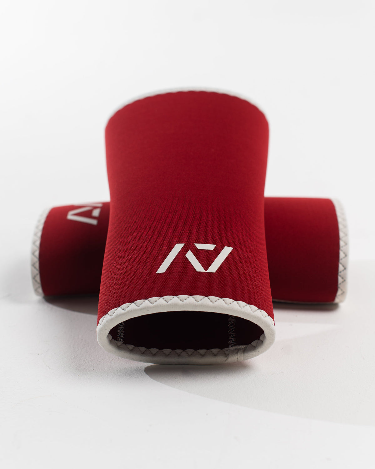A pair of red knee sleeves with a white design that resembles a rose and tusk, symbolizing strength and beauty. The sleeves are designed with a hourglass-shaped center taper fit.